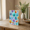 Woodland Whimsy portrait greeting card with orange foxes and colorful trees on a wooden table.
